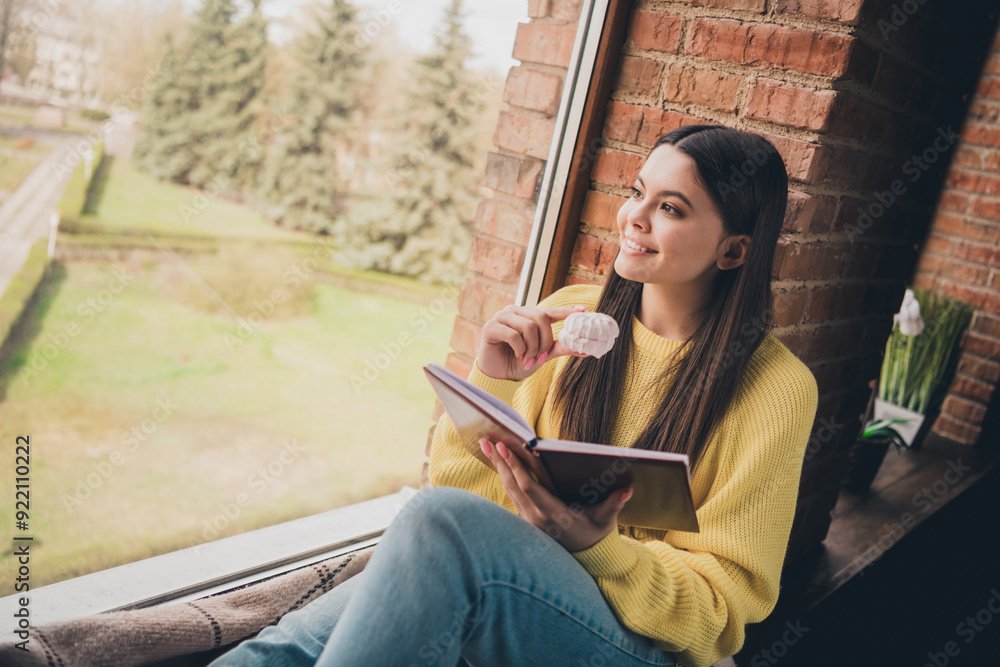 Obraz premium Photo portrait of nice teen lady read book sit windowsill eat snacks dressed yellow garment spend pastime spacious house indoors room