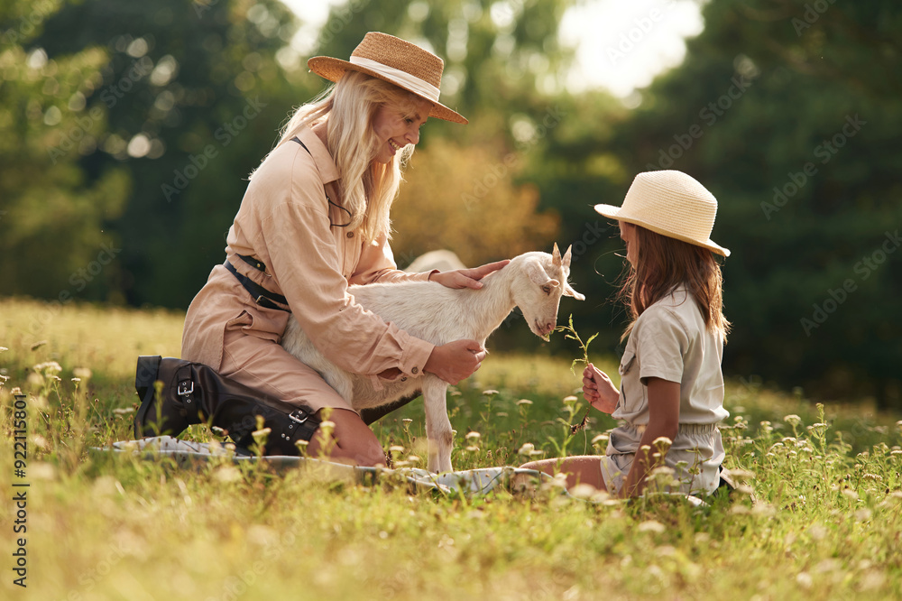 In straw hats. Mother and daughter are together on the farm with goat In straw hats. Mother and daughter are together on the farm with goat