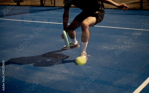 Canvas Print Male padel player in action on blue tennis court with light blue racket, playing