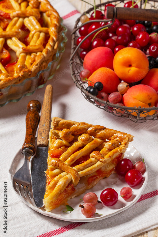 Apricot pie decorated with dough ornament and a metal basket with fruits and berries.