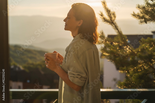 Young woman greeting the morning and sunrise standing on a balcony overlooking the mountains