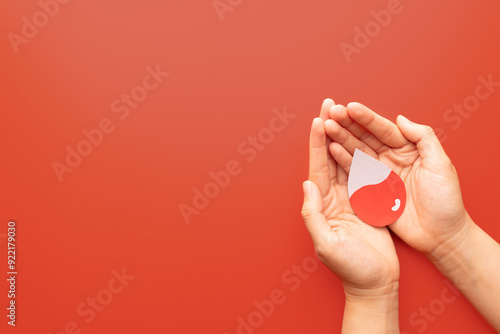 Human hand holding blood drop shape with blood level on red background. Awareness of hematologic disorders such as anemia, sickle cell disease, hemophilia, leukemia and ITP. Blood donation.