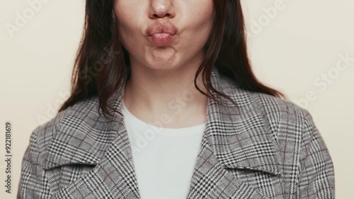 Close-up of a young woman making a humorous face by puffing her cheeks, expressing playfulness and joy on a muted background.