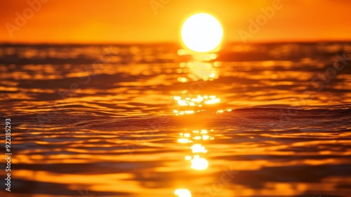 A close-up of the sun setting over a calm sea, with the golden and orange hues reflecting on the watera surface, creating a serene and picturesque scene photo