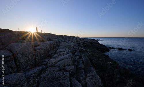 Sunset over rocky coastline near Allinge on the danish island of Bornholm with a lone figure standing on the horizon by the sea. photo