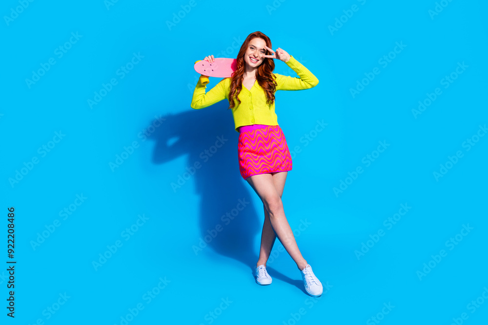 Full body photo of attractive young woman skateboard v-sign dressed stylish yellow clothes isolated on blue color background Full body photo of attractive young woman skateboard v-sign dressed stylish yellow clothes isolated on blue color background