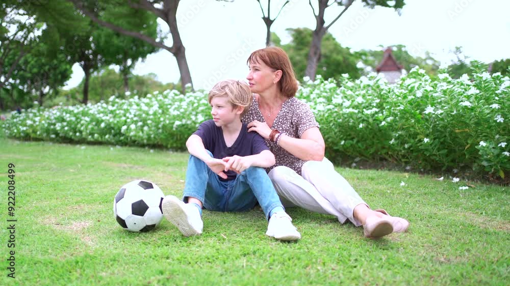 Cheerful caucasian white family relaxing at park, the white boy and grandmother sitting on the grass field at park. Cheerful caucasian white family relaxing at park, the white boy and grandmother sitting on the grass field at park.