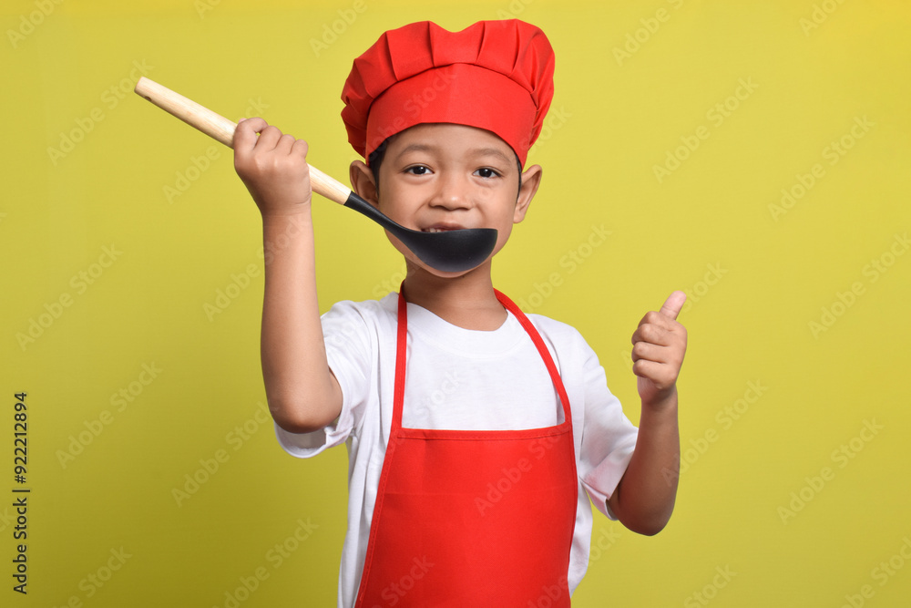 Cute little chef holding ladle isolated on yellow background. Asian boy cooking Cute little chef holding ladle isolated on yellow background. Asian boy cooking