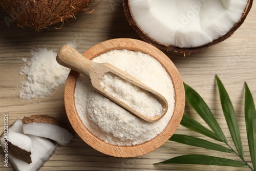 Fresh coconut flour in bowl, scoop, nut and palm leaf on wooden table, flat lay