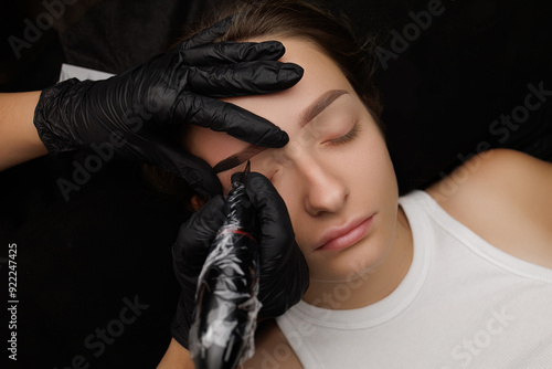 Close-up of the hands of the master who performs the procedure of permanent makeup of eyebrows view from above. Permanent eyebrow makeup PMU for brunettes