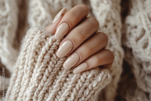Close up of a woman's elegant, nude manicured nails holding a cozy beige knitted sweater. Generated AI