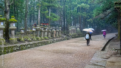 Foto Nara, Japan - 5th March 2018 - visitors with umbrellas at a path with stone lant