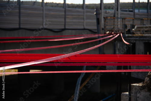 Obraz na płótnie A detailed close-up of tensioned red straps securely fastened with a metal hook on a gravel surface, demonstrating precision and strength in securing elements. w salonie