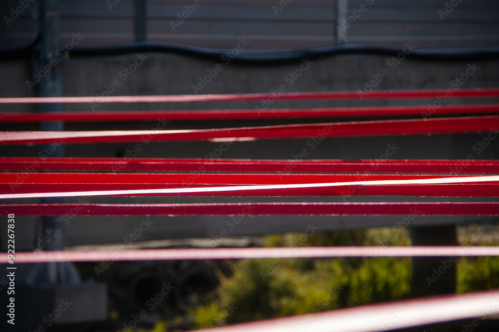 A detailed close-up of tensioned red straps securely fastened with a metal hook on a gravel surface, demonstrating precision and strength in securing elements.