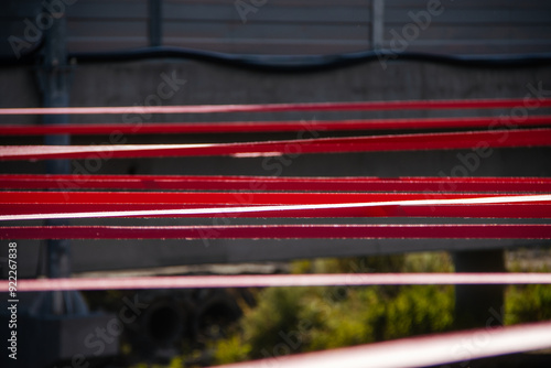 A detailed close-up of tensioned red straps securely fastened with a metal hook on a gravel surface, demonstrating precision and strength in securing elements. photo