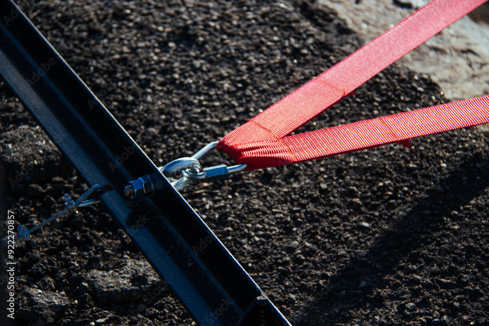A close-up view of a red strap secured with a metal clasp, emphasizing the texture and details of industrial materials. The image captures the strength and precision of the connection.
