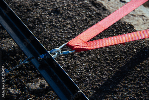 Obraz na płótnie A close-up view of a red strap secured with a metal clasp, emphasizing the texture and details of industrial materials. The image captures the strength and precision of the connection. w salonie
