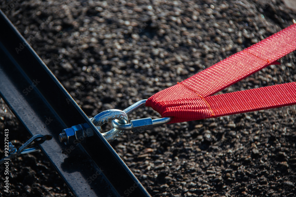 A close-up view of a red strap secured with a metal clasp, emphasizing the texture and details of industrial materials. The image captures the strength and precision of the connection.