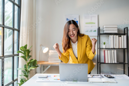 Slika na platnu Asian businesswoman celebrating success raising fists looking at laptop at offic