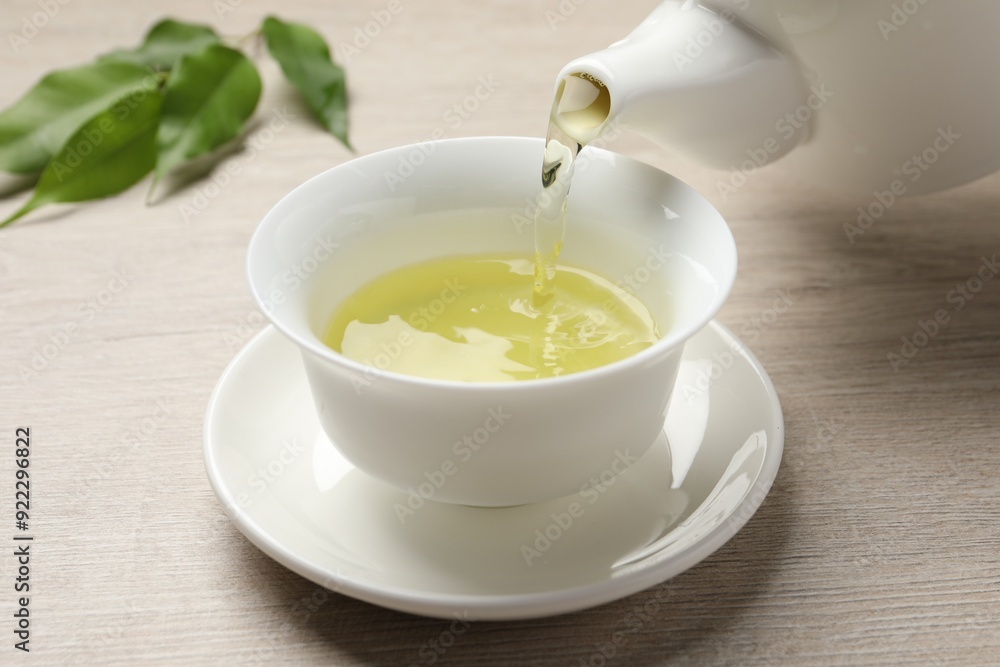 Pouring refreshing green tea into cup at wooden table, closeup Pouring refreshing green tea into cup at wooden table, closeup