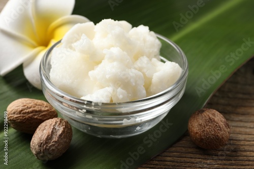 Shea butter in bowl, flower and nuts on wooden table, closeup