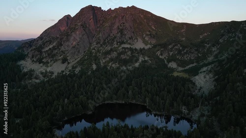 Aerial view of a picturesque alpine lake in a dense spruce forest and a mountain peak in the evening photo