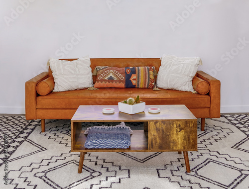 Fotografi Living room with brown leather couch, coffee table, designer southwest rug
