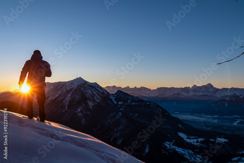 Silhouette of active man with sunrise view of snow capped Dobratsch and mountain range Julian Alps. Ski tour to Kobesnock, Bad Bleiberg, Carinthia, Austria. Remote winter wonderland, Austrian Alps photo