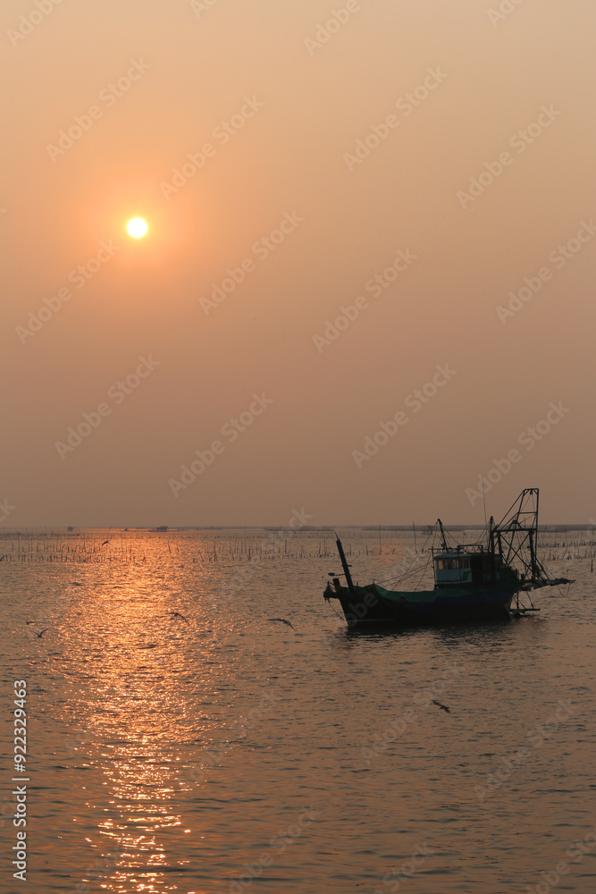 A local fishing boat is moored at sea and the background sunset.