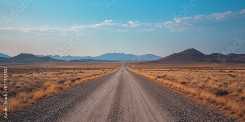 Obraz na płótnie An endless gravel road stretches to the horizon, flanked by barren land and distant mountains, embodying solitude and inviting adventurous exploration in natures tranquil embrace under a vast sky w salonie