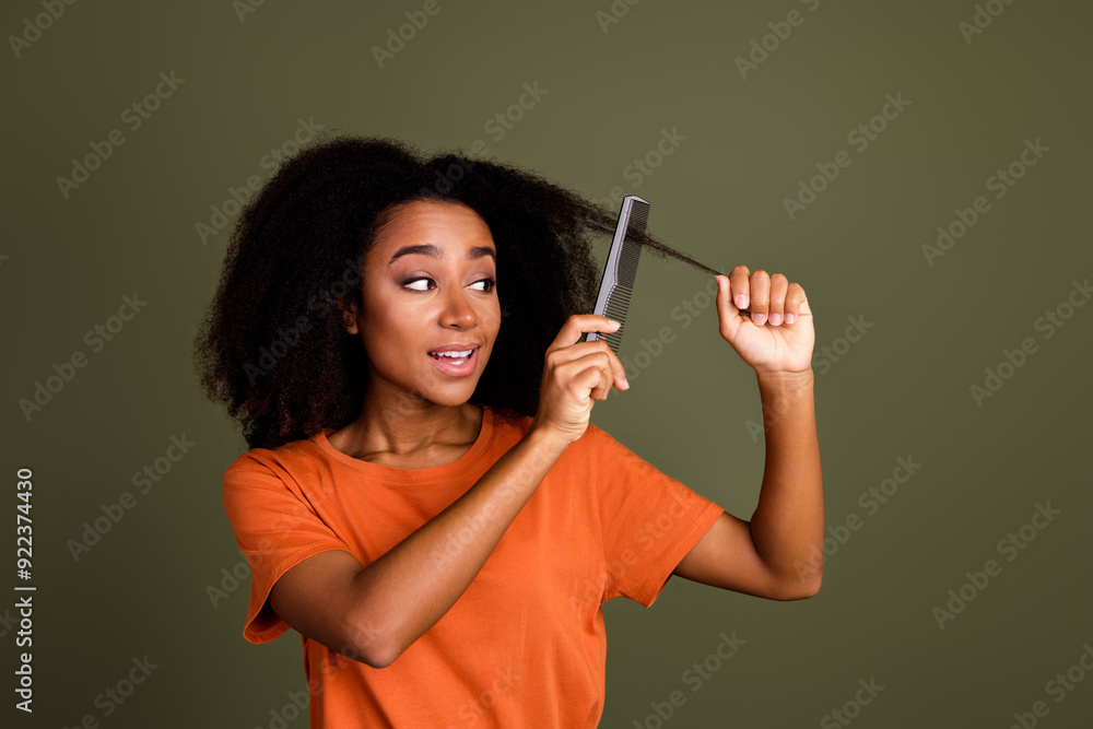 Photo of positive nice woman with perming coiffure dressed orange shirt holding curl comb unruly hair isolated on dark khaki background Photo of positive nice woman with perming coiffure dressed orange shirt holding curl comb unruly hair isolated on dark khaki background