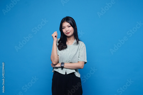 Photo of charismatic Pensive asian young woman with long chestnut hair keeps hands together near chin, has cute expression, wears green shirt