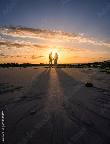 Silhouette of a young couple holding hands on Palmar Beach during sunset in Belle Mare, Mauritius, Africa.