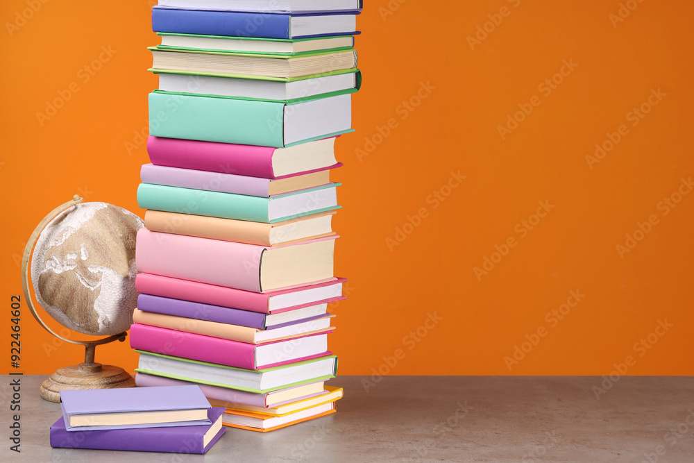 Stack of colorful books and globe on wooden table against orange background, space for text Stack of colorful books and globe on wooden table against orange background, space for text