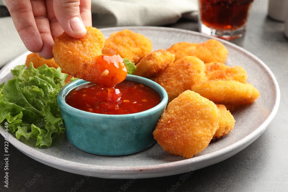 Woman dipping nugget into chili sauce at grey table, closeup Woman dipping nugget into chili sauce at grey table, closeup