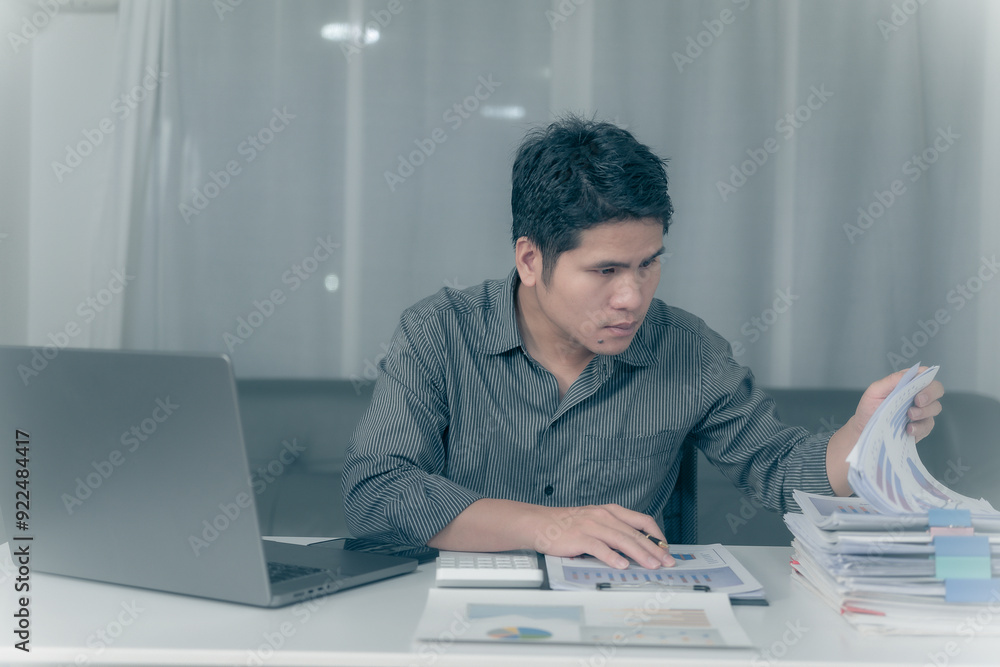 Asian businessman working overtime to analyze finances, working on budget. Calculating with a calculator in the office at night Asian businessman working overtime to analyze finances, working on budget. Calculating with a calculator in the office at night