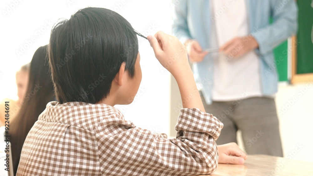 Obraz premium Asian boy sitting and playing with his hair while listen teacher teaching. Professional elementary student think about theory while try to understand idea while teacher explain in lesson. Pedagogy.