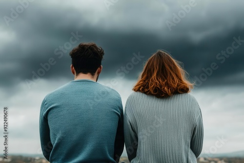 A couple sits together, gazing at a dramatic sky, symbolizing connection and contemplation amidst nature's beauty. photo