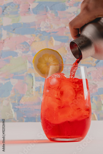 Top of cockatil shaker serving red drink on high ball glass with ice cubes and slice of lemon photo