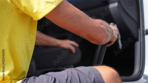 A person squatting uses a vacuum cleaner to clean the carpets and interior of the car. 