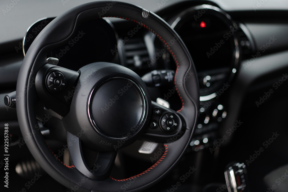 A steering wheel in a car, with a black leather steering wheel cover. The steering wheel is positioned in the center of the image and is black and red. A steering wheel in a car, with a black leather steering wheel cover. The steering wheel is positioned in the center of the image and is black and red.