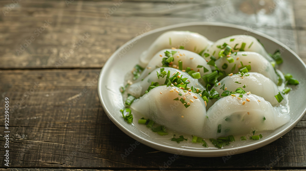 Rustic wooden table with a plate of pork-filled steamed rice dumplings, topped with green onions and sesame seeds Rustic wooden table with a plate of pork-filled steamed rice dumplings, topped with green onions and sesame seeds