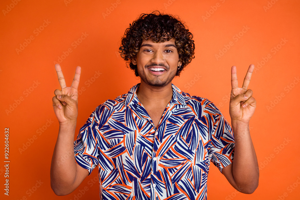 Photo portrait of handsome young man show v-sign dressed stylish colorful garment isolated on orange color background Photo portrait of handsome young man show v-sign dressed stylish colorful garment isolated on orange color background