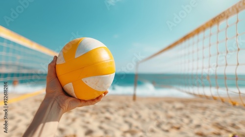 A person is holding a yellow and white volleyball on a beach