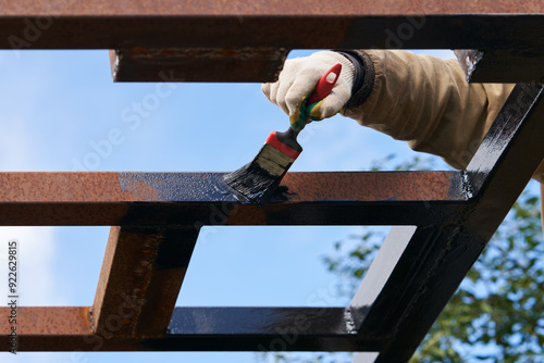 A man applying anti-corrosion primer to a metal structure. Fragment of a man's hand with a molar brush against the sky. photo