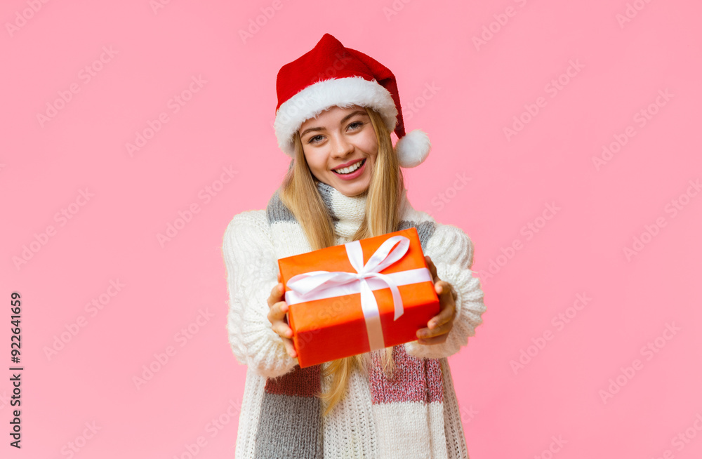 Happy girl in Santa hat giving Christmas present, yellow studio background, empty space Happy girl in Santa hat giving Christmas present, yellow studio background, empty space