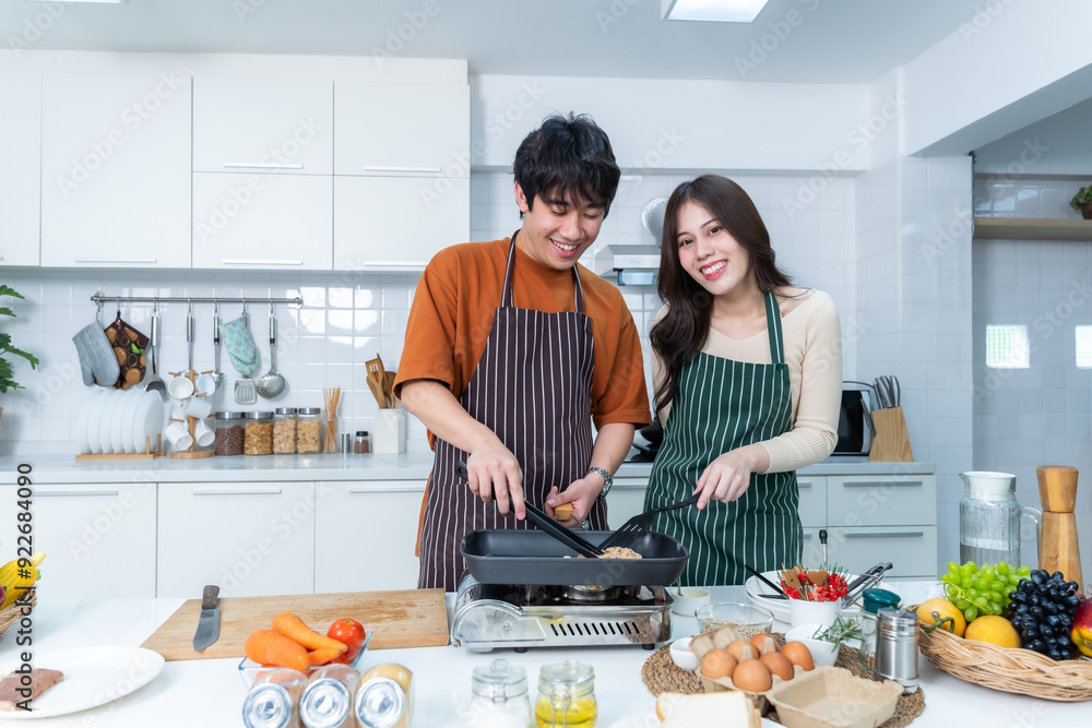 Happy portrait of loving young asian of having fun standing a cheerful preparing food and enjoy cook cooking with vegetables, meat, bread while standing on a kitchen Condo life or home
