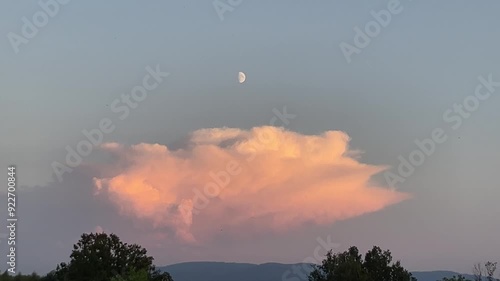 Evening sky with half moon, stormy menacing Anvil cloud, Cumulonimbus incus illuminated in orange by setting sun over hirizon with Silesian Beskids mountains. Topics: storm alert, meteorology, weather photo