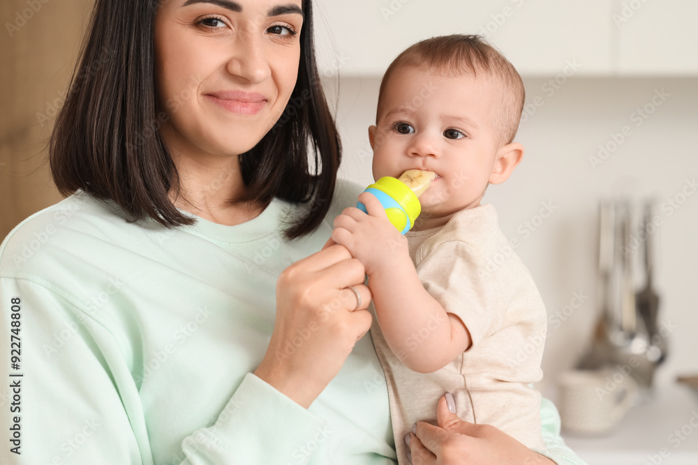 Mother giving her little baby nibbler with food in kitchen, closeup Mother giving her little baby nibbler with food in kitchen, closeup
