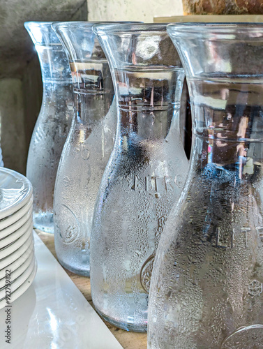 Elegant transparent glass water carafes with condensation on a wooden table in a restaurant setting